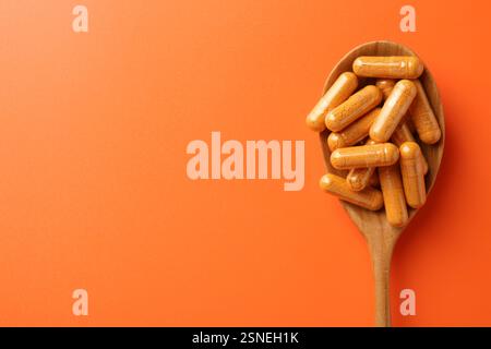 Kurkuma-Kapseln in Holzlöffel auf orangem Hintergrund, Draufsicht Stockfoto