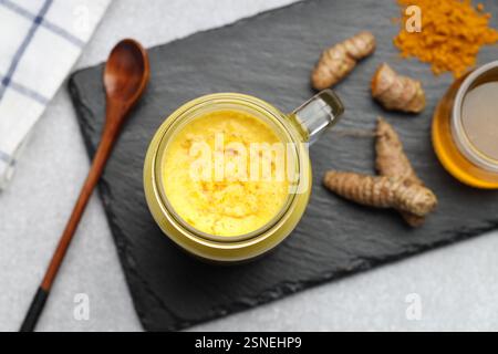 Köstlicher Kurkuma-Latte mit Honig, Pulver und Rhizomen auf grauem Tisch, flach gelegen Stockfoto
