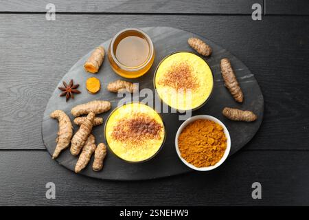 Köstlicher Kurkuma-Latte, Pulver und Rhizome auf schwarzem Holztisch, flach gelegen Stockfoto