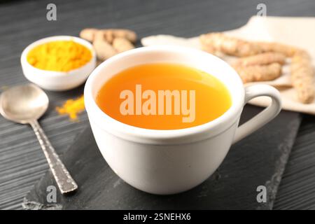 Aromatischer Kurkuma-Tee, Pulver und Rhizome auf schwarzem Tisch, Nahaufnahme Stockfoto