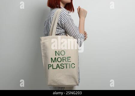 Junge Frau, die Öko-Tasche mit No More Plastic Text auf hellem Hintergrund hält, Nahaufnahme Stockfoto