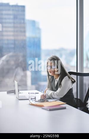 Glückliche reife asiatische Profi-Frau, die im Büro arbeitet, vertikales Porträt. Stockfoto