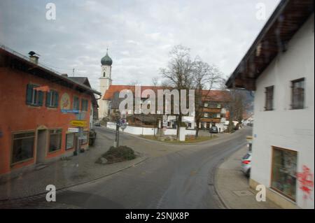 Deutschland, München. Ein kleines bayerisches Dorf mit Kirchturm im Hintergrund schmiegt sich friedlich zwischen Bergen. Dieses szenische Bild weckt einen Sinn Stockfoto