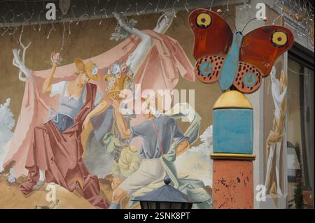 In Deutschland, München, zeigt ein Wandgemälde ein hell gekleidetes Paar, das neben einem bunten Schmetterling steht, der auf einer Stange thront. Die Szene dient als Erinnerung o Stockfoto