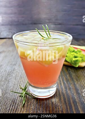 Mit Rhabarber und Rosmarin in ein Glas Limonade, die Stiele und Blätter von Rhabarber auf einem hölzernen Brettern Hintergrund Stockfoto