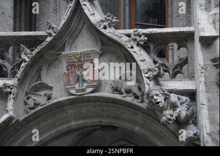Ein kunstvoller Steinbogen in München, Deutschland, zeigt komplizierte Schnitzereien und ein Wappen, das gotische Architektur und mittelalterliche Handwerkskunst zeigt. Stockfoto