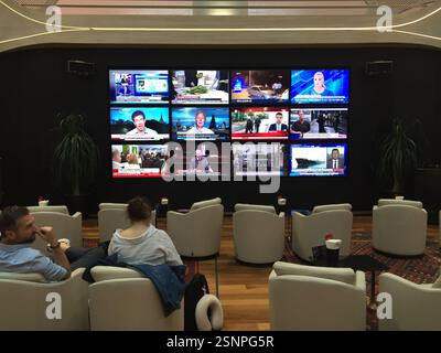 Business Lounge am Flughafen mit komfortablen Sitzgelegenheiten. Die Leute entspannen sich auf den Sofas und arbeiten an ihren Laptops. Es gibt auch mehrere Fernsehbildschirme A Stockfoto
