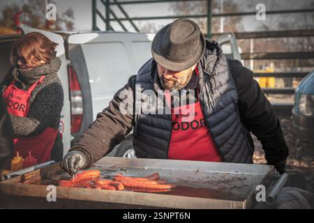 BACKI PETROVAC, SERBIEN - 7. FEBRUAR 2025: Ein Verkäufer in Backi Petrovac, Serbien, grillt kobasica-Würstchen auf einer traditionellen Balkanrostilj. Das Zwitschern Stockfoto