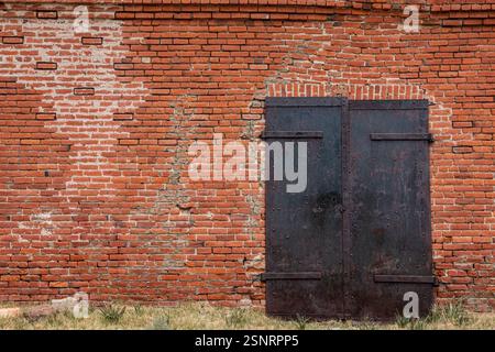 Schwere Stahltüren an der Seite eines Lagerhauses aus rotem Backstein in Bodie Ghost Town. Die Textur und die Ziegel bilden einen interessanten Hintergrund. Stockfoto