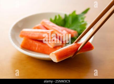 Nachgeahmte Krabbenstäbchen mit Essstäbchen auf einem Holztisch Stockfoto