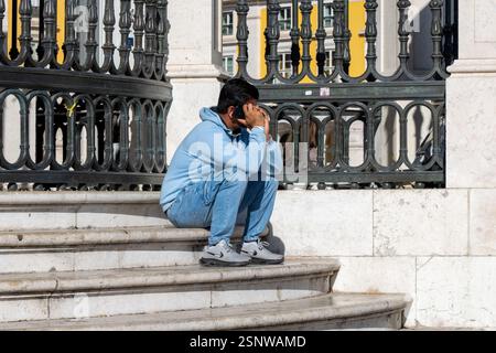 Lissabon Portugal - 28. September 2024: Mann sitzt auf Stufen vor der Tür und spricht auf einem Handy in Lissabon Portugal Stockfoto