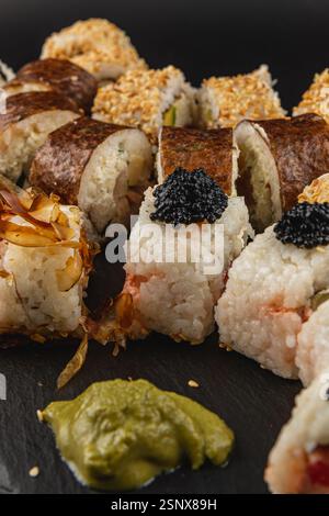 Eine wunderschön angeordnete Sushi-Platte zeigt eine Vielzahl von Sushi-Brötchen, einschließlich Garnelen und Gemüse, garniert mit Wasabi und Kaviar. Die schwarzen s Stockfoto