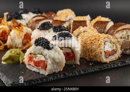 Eine Vielzahl von Sushi-Rollen auf einer dunklen Steinoberfläche mit verschiedenen Füllungen und Belägen. Leuchtende Farben und einzigartige Texturen sorgen für ein klares Bild Stockfoto