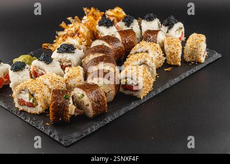 Eine raffinierte Sushi-Platte zeigt eine Vielzahl von Brötchen, einschließlich solcher mit Kaviar und Sesam. Das dunkle Schieferbrett steht im Kontrast zum hellen Stockfoto