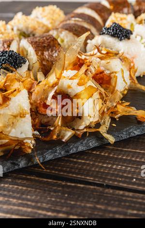 Eine Vielzahl von Gourmet-Sushi-Brötchen sind kunstvoll auf einer dunklen Steinplatte angeordnet. Die Rollen verfügen über einzigartige Beläge wie Kaviar und zarte Späne Stockfoto