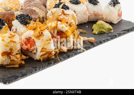 Eine wunderschön angeordnete Sushi-Platte zeigt verschiedene Brötchen mit Fischrogen und Kokosflocken, serviert mit Wasabi auf einem Schieferbrett in einem Moder Stockfoto