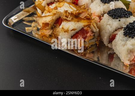Frische Sushi-Brötchen sind kunstvoll auf einer Silberplatte angeordnet. Die Rollen sind mit knusprigen Flocken und schwarzem Kaviar belegt, was eine Kombination aus Tex darstellt Stockfoto