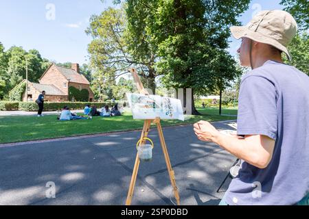 Ein Künstler betrachtet sein Aquarellbild auf einer Staffelei, während er eine Szene von Cook's Cottage in Fitzroy Gardens, Melbourne, malte Stockfoto