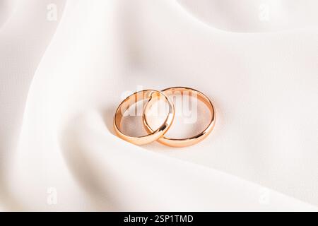 Zwei goldene Eheringe liegen auf weichen Falten aus elegantem Seidenstoff. Wunderschönes Hochzeitsdesign. Eine Kopie des Bereichs. Hochzeitshintergrund Stockfoto