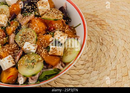 Ein lebendiger Salat mit einer Mischung aus frischem Gemüse, einschließlich Gurken und Mango, garniert mit Sesamsamen und Käsewürfeln. Es wird in einer de serviert Stockfoto