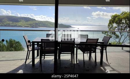Balkon mit Meerblick. Korbmöbel auf einem Holzbalkon mit Blick auf das glitzernde Meer. Ruhiger Zufluchtsort. Idealer Ort für Kaffee am Morgen oder e Stockfoto