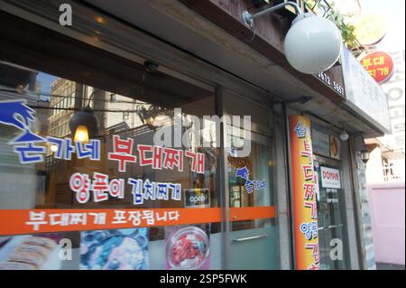 Koreanisches Restaurant Südkorea. Hangeul-Text. Orangefarbene und weiße Schilder. Armee Eintopf Kimchi Eintopf. Zum Mitnehmen verfügbar in Südkorea. Stockfoto