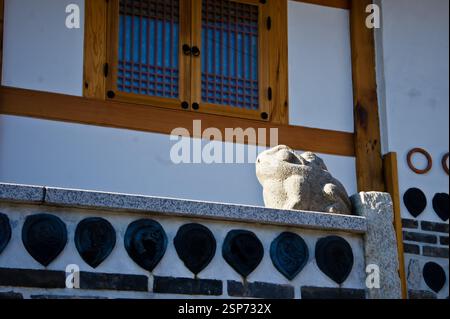 Steinfroschskulptur auf einer Wand mit traditionellem koreanischem Fenster im Hintergrund. Südkorea ist bekannt für sein reiches kulturelles Erbe, und dies Stockfoto
