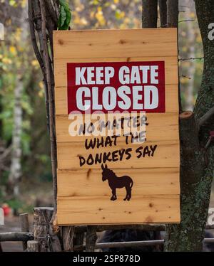 Ein hölzernes Schild auf einem Baum mit der Aufschrift „KEEP GATE CLOSED, egal was die Esel sagen“ Stockfoto