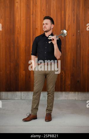 Der talentierte junge Musiker posiert selbstbewusst mit einer Trompete im Freien Stockfoto