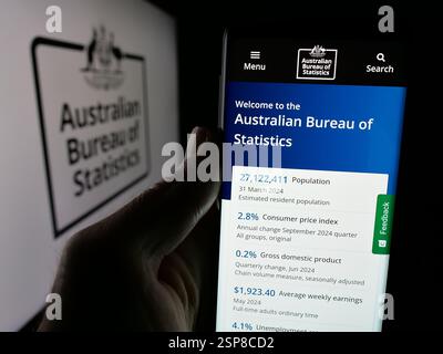 In dieser Fotoabbildung hält eine Person ein Handy mit der Webseite der Agentur Australian Bureau of Statistics (ABS) auf dem Bildschirm vor dem Logo. Stockfoto