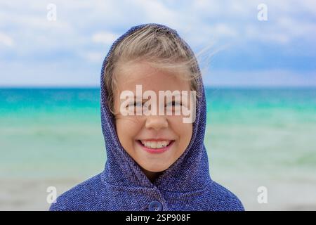 Porträt eines lächelnden kaukasischen Kindes 7 8 Jahre in der Kapuze bei windigem Wetter auf Meereshintergrund Stockfoto