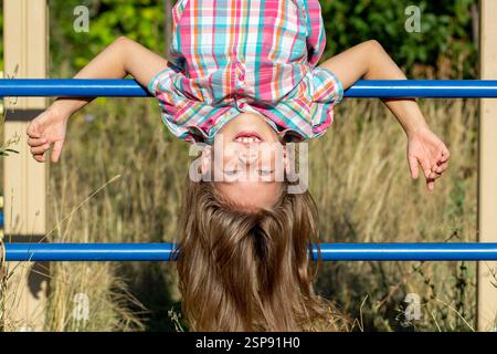 Porträt eines lächelnden kaukasischen Kindes von 7 bis 8 Jahren, das kopfüber an Wandstangen hängt Stockfoto