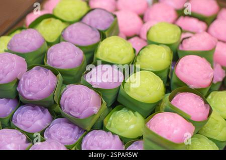 Nahaufnahme zarter, rosafarbener thailändischer Gelee-Desserts in sanften Pastelltönen – Rosa, Grün und Lila – in kleinen Bechern mit Bananenblättern verpackt. Stockfoto