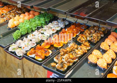Nahaufnahme verschiedener Sushi-Sorten, die an einem Street Food-Stand gezeigt werden, mit Algensalat, Oktopus, Muscheln, Lachsrogen, und gegrillter Aal. Stockfoto
