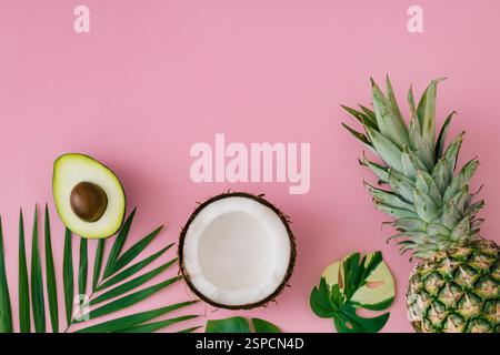 Kreatives Layout mit Ananas, Kokos, Avocado und grünen tropischen Blättern auf hellrosa Hintergrund. Sommer tropische Früchte und Blätter Idee. Stockfoto