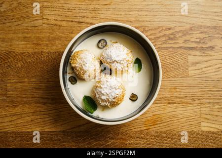 Goldene, knusprig gebratene Hüttenkäse-Knödel, mit Puderzucker bestäubt, serviert in einer Schüssel mit cremiger Vanillesauce. Garniert mit frischen Minzblättern Stockfoto