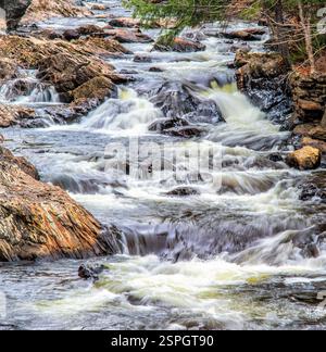Ein malerischer Fluss stürzt über felsige Kaskaden und erzeugt einen faszinierenden Wasserfall-Effekt, umgeben von zerklüfteten Steinen und Waldvegetation. Stockfoto