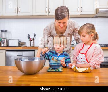 Eine Mutter und ihre beiden Kinder bereiten gemeinsam Essen in einer gemütlichen Küche zu. Spaß und Engagement erfüllen die Atmosphäre, während sich die Familie durch die Welt zieht Stockfoto