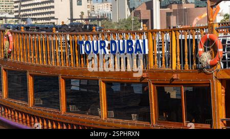 Dubai, VAE - 13. November 2024: Traditionelle hölzerne Dhow mit „Tour Dubai“-Schildern in Dubai Creek, VAE. Das Boot zeigt Kulturerbe, Tourismus und Stadtlandschaft Stockfoto