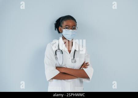 In Schutzmaske. Die junge afroamerikanische Frau steht vor weißem Hintergrund. Stockfoto