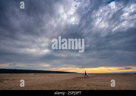 Einzelnes Pferd und Reiter bei Sonnenuntergang am leeren Strand unter stürmischem Himmel Stockfoto