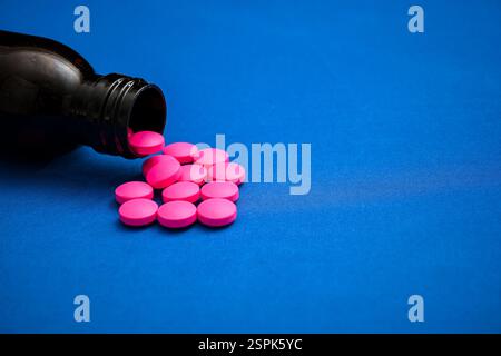 Pinkfarbene Pillen aus einer dunklen Arzneiflasche auf blauem Hintergrund erzeugen einen auffälligen Kontrast. Stockfoto