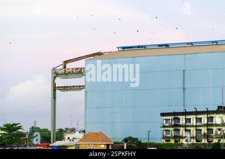 Industrie-Lagergebäude mit einer großen wellplattenartigen blauen Metallwand und verwittertem Stahlkonstruktionsrahmen unter einem bewölkten Himmel. Stockfoto