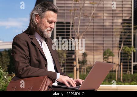 Mann in elegantem Anzug mit Laptop auf dem Stadtplatz Stockfoto