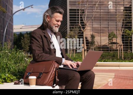 Mann in elegantem Anzug mit Laptop auf dem Stadtplatz Stockfoto