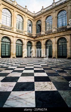 Ein wunderschön gestalteter Innenhof mit kariertem Marmorboden und großen Bogenfenstern. Die Architektur zeigt klassische Elemente mit einer Mischung Stockfoto