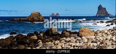 Ein malerischer Blick auf die Küste mit felsigen Formationen, Wellen, die an der Küste zusammenbrechen, und fernen Inseln unter einem klaren blauen Himmel. Stockfoto