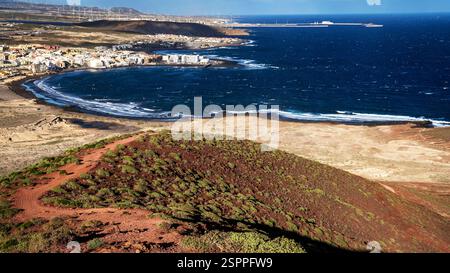 Ein malerischer Blick auf eine Küstengegend mit Sandstrand, Wellen, die am Ufer krachen, und eine kleine Stadt mit weißen Gebäuden. Die Landschaft umfasst einen Stockfoto