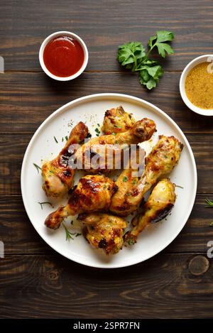 Barbecue mit gebratenen Hähnchenkeulen, serviert mit Sauce. Brauner Holzhintergrund, Draufsicht, flache Lage Stockfoto