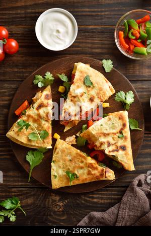 Leckere Hühnchen Quesadillas mit frischem Gemüse auf Servierbrett auf braunem Holztisch. Draufsicht, flach Stockfoto